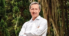 a man standing in front of trees with his arms crossed