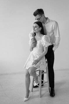 a man standing next to a woman on top of a stool in front of a white wall