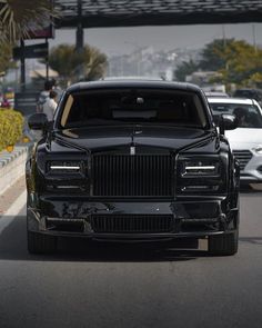 a black car is parked on the side of the road with other cars behind it