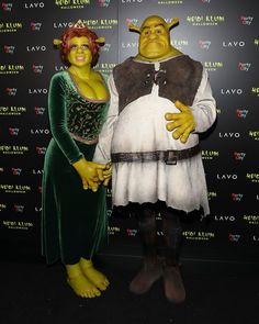 two people in costumes standing next to each other on a black carpeted area with a wall behind them