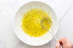 a person whisking olive oil in a white bowl