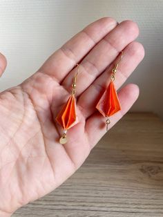 a hand holding an orange pair of earrings