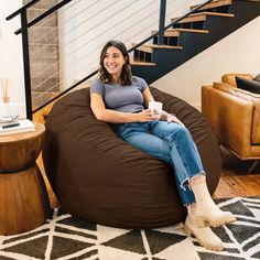 a woman sitting on a bean bag chair with a cup in her hand and smiling at the camera