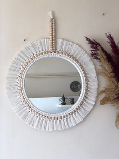 a round mirror hanging on the wall next to some dried plants and a plant pot