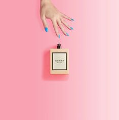 a person's hand reaching for a bottle of gucci perfume on a pink background