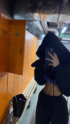 a woman taking a selfie in front of lockers with her phone up to her face