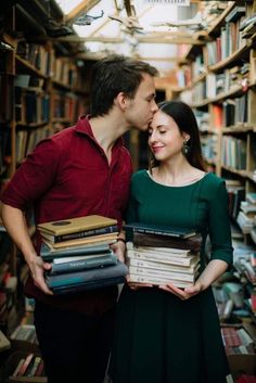 a man and woman standing next to each other holding books in front of a library full of books