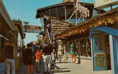 an old photo of people walking down the street in front of shops and stores on stilts