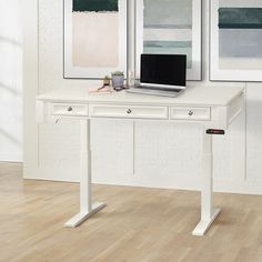 a white desk with a laptop on it in front of two framed pictures and a wooden floor