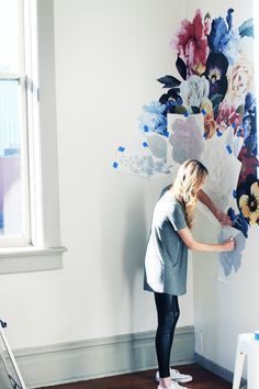 a woman is painting flowers on the wall