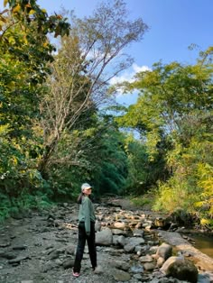 a woman standing on rocks in the middle of a river with trees and bushes around her