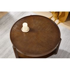 a round wooden table with a white candle on it's top, sitting on a gray rug