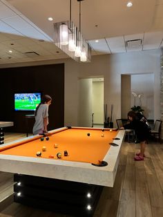 two children playing pool in a large room with an entertainment center on the other side