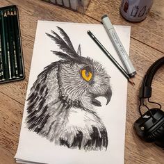 a drawing of an owl with yellow eyes sits on a table next to some crayons