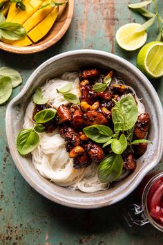 a bowl filled with noodles and meat on top of a table next to sliced limes