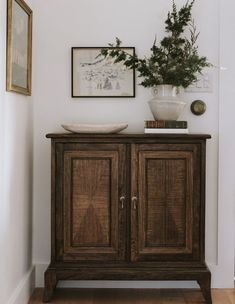 a wooden cabinet sitting in the corner of a room next to a potted plant