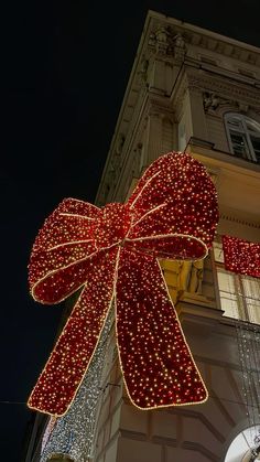 a large red bow hanging from the side of a tall building with lights on it