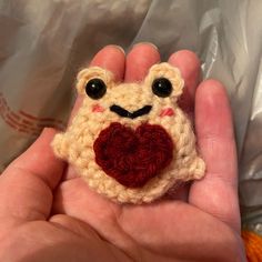 a hand holding a small crocheted frog with a heart on it's chest