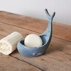 a soap dish with a white ball in it on a wooden table next to a roll of toilet paper