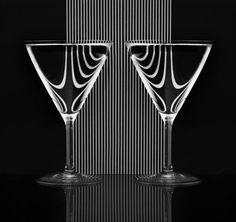 two wine glasses sitting next to each other on a black surface with lines in the background