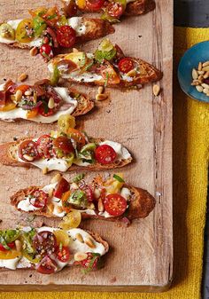 a wooden cutting board topped with slices of bread covered in toppings