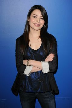 a woman standing in front of a blue wall with her arms crossed and looking at the camera