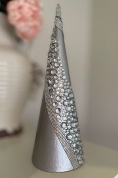 a silver cone shaped object sitting on top of a white table next to a vase