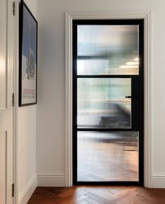 an empty room with a black door and wooden flooring on the other side of it