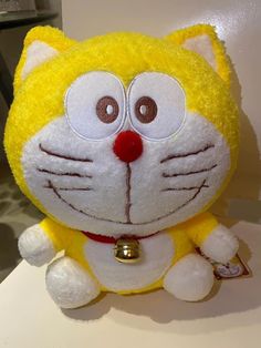 a yellow and white stuffed cat sitting on top of a table next to a wall