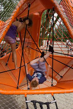 two people are playing in an orange play structure with ropes and netting on the ground