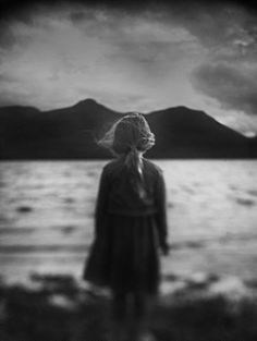 a woman standing on top of a beach next to the ocean under a cloudy sky