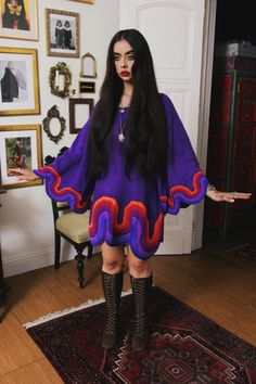 a woman with long black hair in a purple dress and boots standing on a rug