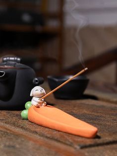 a small figurine sitting on top of a wooden table next to a teapot