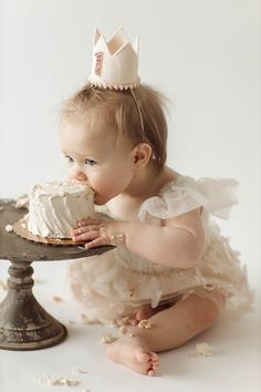 a baby is sitting on the floor with a cake in front of her face and wearing a tiara