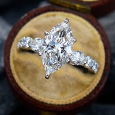 an oval shaped diamond ring with three pear shaped diamonds on the band in a wooden box