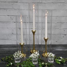 three candles are sitting on a table with flowers and greenery