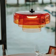 a red light hanging over a table with wine glasses on it and water in the background