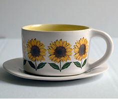 a yellow and white coffee cup with sunflowers painted on the side, sitting on a saucer