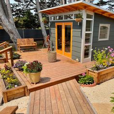 a wooden deck with potted plants on it next to a small house and trees