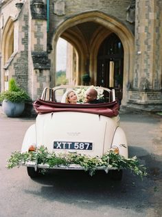 a man and woman sitting in an old fashioned car with greenery on the back