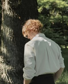 a woman standing in front of a tree with her back turned to the camera, wearing a white shirt and black skirt