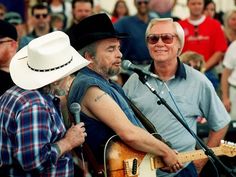 two men are playing guitar and singing into microphones in front of a large crowd