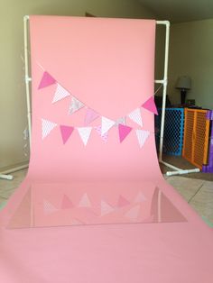 a pink backdrop with bunting flags and streamers on the top, in front of a tiled floor