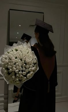 a woman holding a bouquet of white roses in front of a mirror with a graduation cap on her head