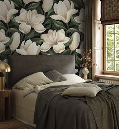 a bed sitting in front of a window next to a wall with flowers on it