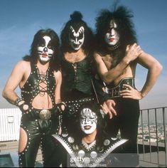 the kiss band posing for a photo on top of a building with their faces painted white