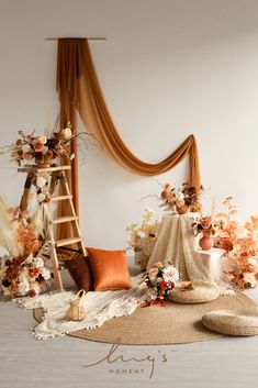 an arrangement of flowers and decorations on the floor in front of a ladder, with a backdrop draped over it