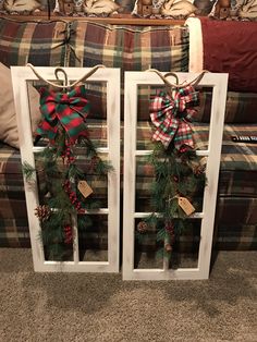 two white windows decorated with christmas wreaths and pine cones are sitting on the floor in front of a couch