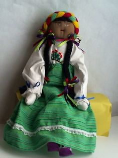 a doll is sitting on a white surface with a green dress and colorful headdress