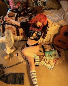 a woman with red hair sitting on the floor next to a fan and some books